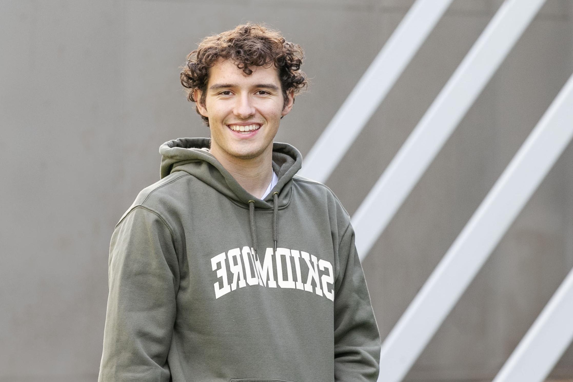 Braedon Quinlan ’24 smiles at the camera while wearing a Skidmore sweatshirt in front of the Tang Teaching Museum.